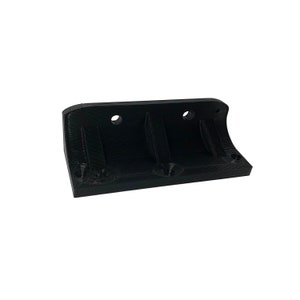 May include: A black, 3D-printed object with a rectangular base and curved edges. It features two circular holes and two recessed slots. The object is designed for mounting or holding other items.