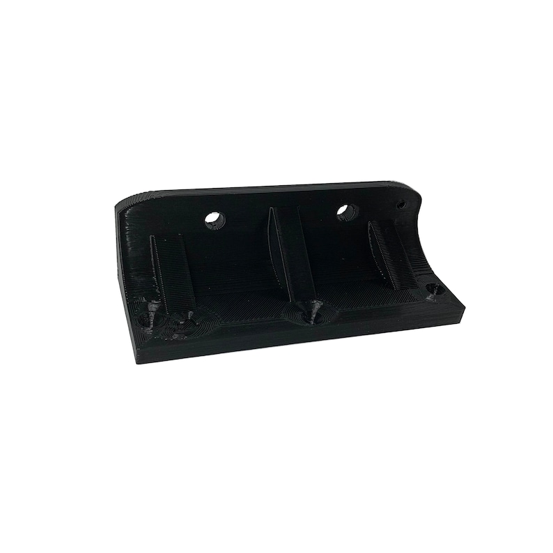 May include: A black, 3D-printed object with a rectangular base and curved edges. It features two circular holes and two recessed slots. The object is designed for mounting or holding other items.
