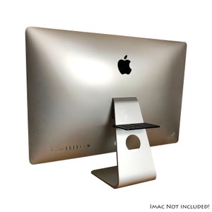 May include: A silver computer monitor stand with a black shelf. The stand has a hole in the back for cable management.  IMAC NOT INCLUDED!