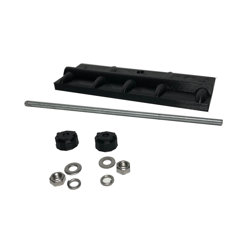 May include: A black, rectangular component with four rounded protrusions, a threaded rod, two black knobs, washers, and nuts. The components are arranged on a white background, suggesting a hardware or mechanical assembly.
