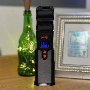 May include: Black Venty vaporizer with an orange accent, the word "Venty" is printed on the device. The device has a digital display that reads "ECO". The text "Docking stand Only" is printed at the bottom. The text "No cable is included!" is printed at the top.