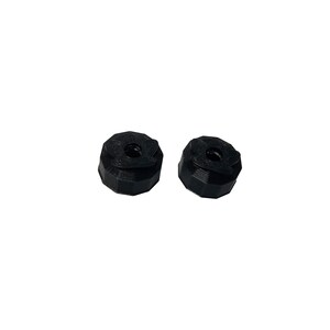 May include: Two black, 3D-printed objects with a geometric design. Each object has a central hole and a multi-faceted exterior. The objects are set against a plain white background.