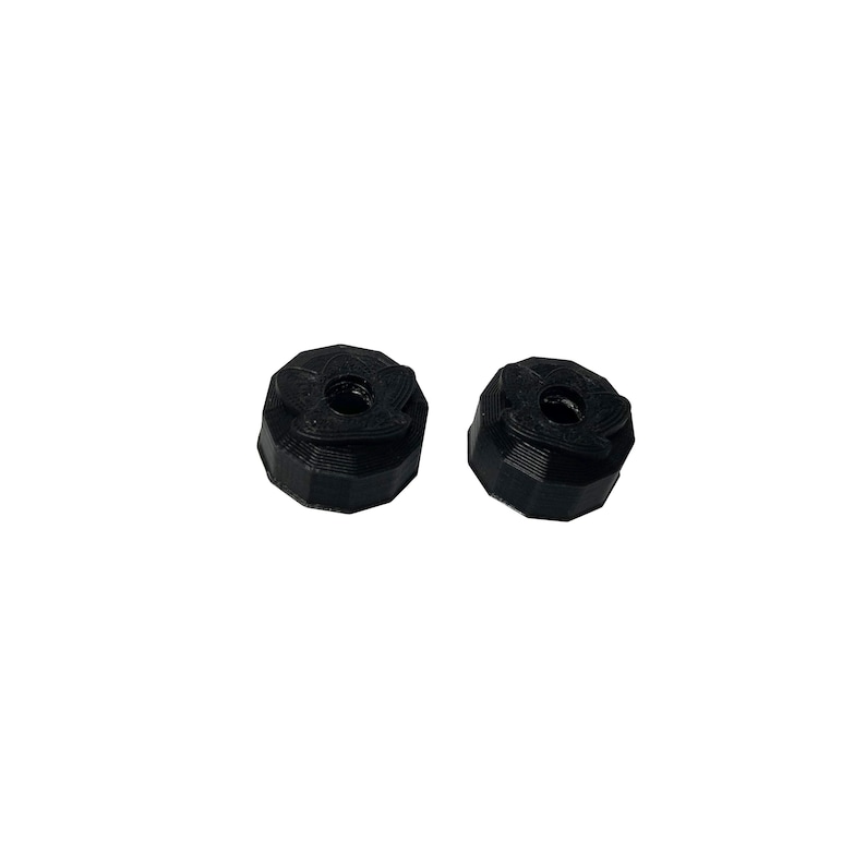 May include: Two black, 3D-printed objects with a geometric design. Each object has a central hole and a multi-faceted exterior. The objects are set against a plain white background.