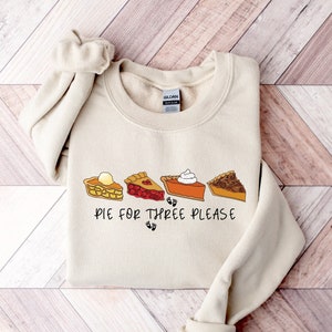 May include: A beige sweatshirt with a graphic of four different pie slices and the text "Pie for three please".