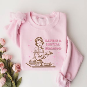 Peut inclure: Sweat-shirt rose avec une illustration r&eacute;tro d'une femme tenant une tarte et le texte "Having a mental Bakedown".