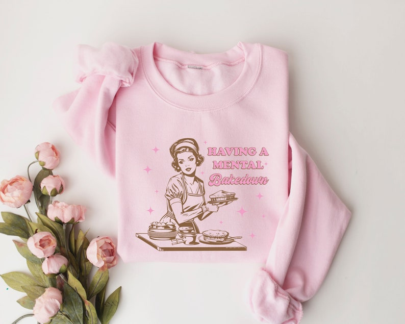 Peut inclure: Sweat-shirt rose avec une illustration r&eacute;tro d'une femme tenant une tarte et le texte "Having a mental Bakedown".