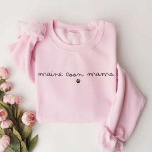 May include: Pink sweatshirt with the text "maine coon mama" and a paw print.