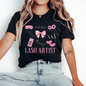 Pu&ograve; includere: Una maglietta nera con un design rosa e nero di strumenti per ciglia e il testo "LASH ARTIST".