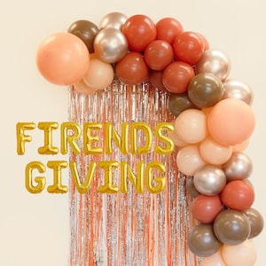 Peut inclure: Une arche de ballons aux tons pêche, marron et argent, avec une frange orange et argent. Des ballons en aluminium dorés épellent "FRIENDS GIVING", parfait pour une célébration de Thanksgiving ou de Friendsgiving.