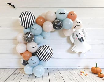 May include: A balloon arch featuring a mix of light blue, orange, white, and black balloons, including two large black and white striped spheres and a white ghost-shaped foil balloon. Small black bat cutouts are attached to several balloons.