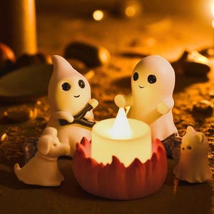 Puede incluir: Una escena de Halloween con figuras de fantasmas blancos con ojos negros y sonrisas. Un candelabro rojo y blanco con una vela encendida está en el centro. También hay una pequeña figura de perro blanco.