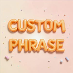 May include: Orange inflatable balloons spelling out "CUSTOM PHRASE" on a light pink background. The balloons are arranged in two rows, with "CUSTOM" above "PHRASE". Small confetti and decorative elements are scattered around the text.