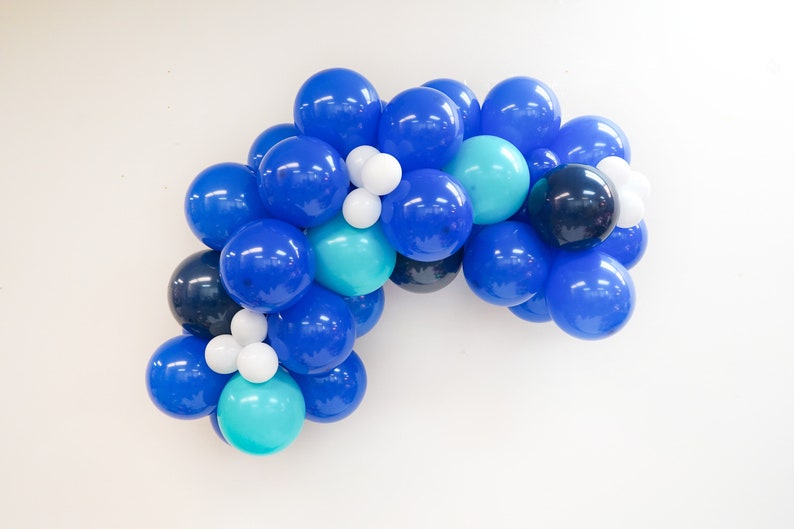 K&ouml;nnte beinhalten: Eine blaue, t&uuml;rkisfarbene und wei&szlig;e Ballon-Girlande. Die Girlande besteht aus verschiedenen Gr&ouml;&szlig;en von Ballons. Die Ballons sind in einer Halbkreisform angeordnet.