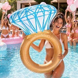 May include: A large inflatable ring-shaped pool float with a gold band and a blue diamond-shaped top. A woman in a white bikini holds the float in a swimming pool, smiling. Other women are in the background, some holding pink balloons.