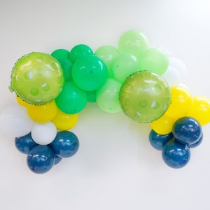 May include: A green, yellow, white, and blue balloon garland. The balloons are arranged in a semi-circle shape. The green balloons have a polka dot pattern.