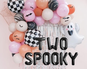 May include: A balloon arch featuring pink, orange, white, and black marble balloons, checkered patterns, and bat decals. A white ghost balloon is on the right. Black foil balloons spell out the text TWO SPOOKY over silver fringe curtains.