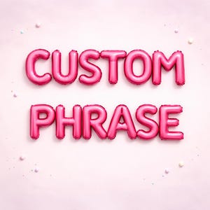 May include: Pink foil balloons spelling out "CUSTOM PHRASE" against a light pink background. The balloons are inflated and have a shiny metallic finish. Small, colorful confetti dots are scattered around the text, adding a festive touch.