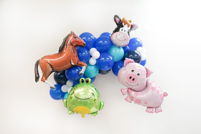 K&ouml;nnte beinhalten: Ein Ballonbogen mit blauen, wei&szlig;en und t&uuml;rkisfarbenen Ballons. Der Bogen enth&auml;lt tierf&ouml;rmige Ballons, darunter ein Pferd, eine Kuh, ein Schwein und ein Frosch.