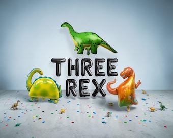 May include: A festive birthday scene with dinosaur-shaped balloons and confetti. The phrase "THREE REX" is spelled out in black balloons. A green Brontosaurus, a yellow Triceratops, and an orange T-Rex balloon are featured.