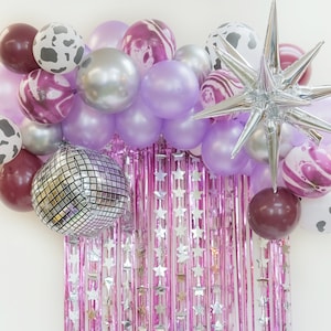 May include: A purple, pink, and silver balloon garland with a silver star balloon. The garland is decorated with cow print balloons, marble print balloons, and disco ball balloons.
