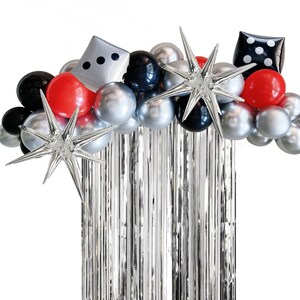 May include: A silver and black balloon arch with red balloons, silver stars, and a dice-shaped balloon. The arch is decorated with silver tinsel streamers.
