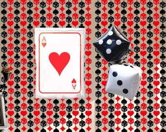 May include: A decorative wall with a repeating pattern of playing card suits and dice. A large Ace of Hearts card balloon and two dice balloons, one black and one white, are featured. The background is a beige color.