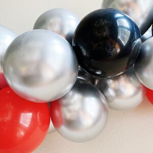 May include: A garland of silver, black, and red balloons. The balloons are shiny and reflect light.