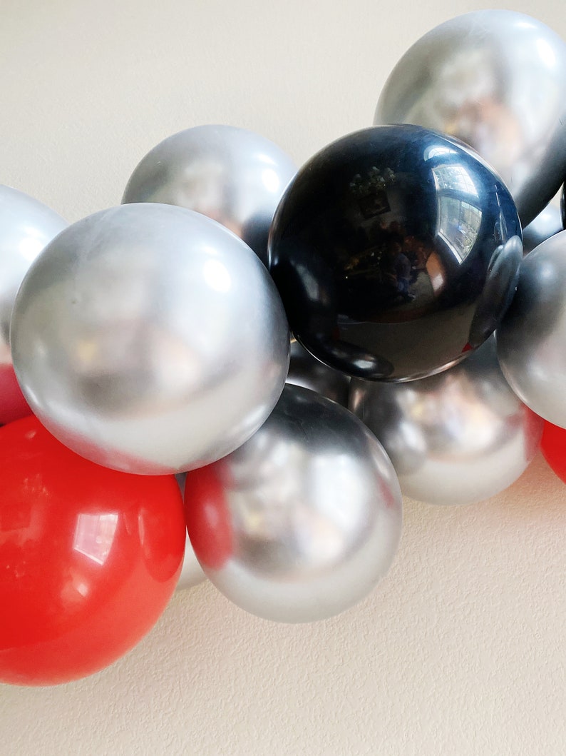 May include: A garland of silver, black, and red balloons. The balloons are shiny and reflect light.