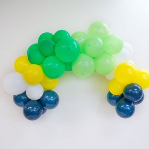 May include: A balloon arch made of green, yellow, white, and blue balloons. The balloons are arranged in a semi-circle shape.