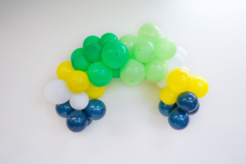 May include: A balloon arch made of green, yellow, white, and blue balloons. The balloons are arranged in a semi-circle shape.