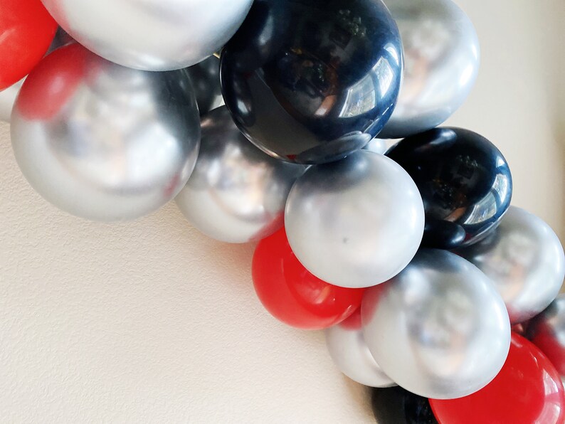 May include: A balloon garland with silver, black, and red balloons. The balloons are arranged in a cascading pattern.