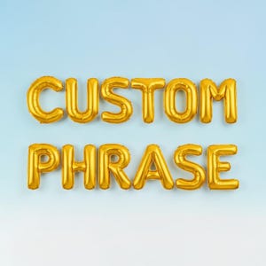 May include: Gold foil balloons spelling out "CUSTOM PHRASE" against a light blue gradient background. The balloons are inflated and have a shiny, metallic finish, perfect for a party or event.