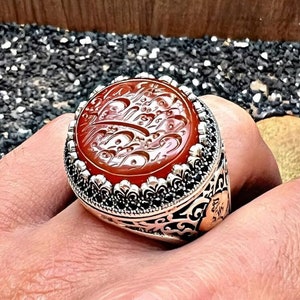 Op de afbeelding: Een zilveren ring met een sierlijk ontwerp heeft een grote, ronde, rode carneol-steen met ingewikkelde Arabische kalligrafie.