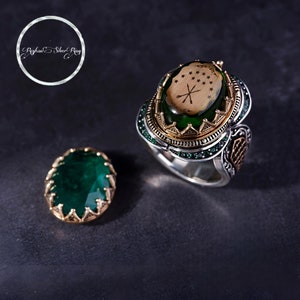 Pode incluir: Um anel de prata com uma gema verde e uma configuração de ouro. A gema tem um design esculpido de uma estrela e uma cruz. O anel é definido com gemas verdes menores ao redor da banda.