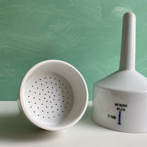Puede incluir: Un embudo de porcelana blanca con una base perforada y un largo pico. El embudo está etiquetado con "KPM Berlin" y "BN 2".