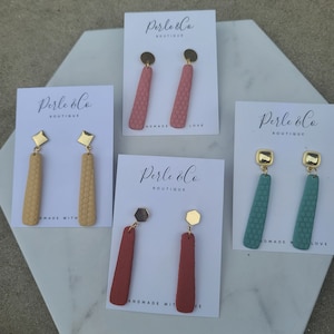Può includere: Tre paia di orecchini fatti a mano in argilla polimerica con dettagli dorati. Gli orecchini sono esposti su cartoncini bianchi con il testo "Perle & Co Boutique" e le parole "Fatto a mano con amore".