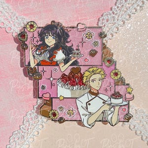 May include: A pink enamel pin featuring two anime-style characters. One character is a woman holding a small cake, and the other is a man holding a cake. The pin has a pink background with floral and heart accents.