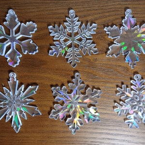 May include: Six iridescent snowflake ornaments with a holographic finish. The snowflakes are made of clear plastic and have a variety of designs.