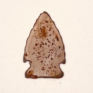 May include: A rusty metal arrowhead with a brown patina. The arrowhead is isolated on a white background.