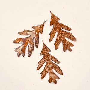 May include: Three rusty metal oak leaves, each with a unique shape and texture, are arranged in a cluster on a white background.