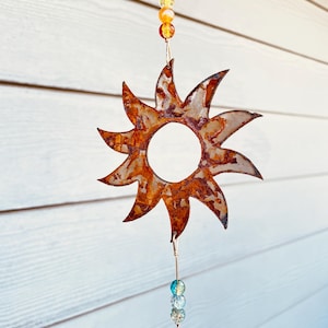 May include: A rusty metal sun with a circular center and a chain with orange and blue glass beads hanging from it.