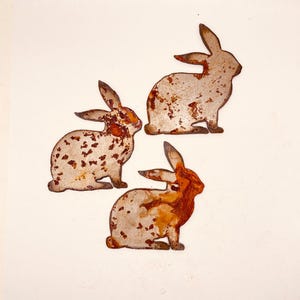 May include: Three metal rabbit silhouettes with a rustic, rusty finish. The rabbits are in various poses and are a great addition to any home decor.