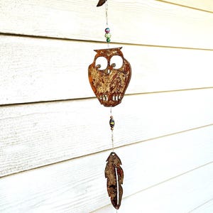 May include: A metal wind chime with an owl, a crescent moon, and a feather. The chime is decorated with beads and a bell at the bottom.