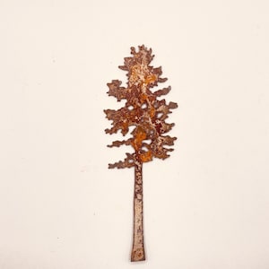 May include: A rusty metal silhouette of a pine tree with a brown and orange patina. The tree is cut out of metal and has a simple, elegant design.