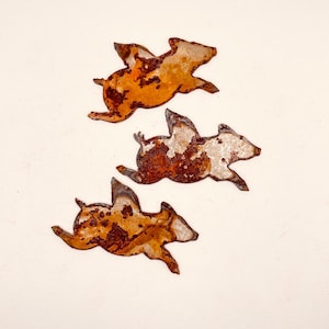 May include: Three rusty metal pig silhouettes, each with a different pose, are arranged on a white background. The pigs are all facing the right side of the image.