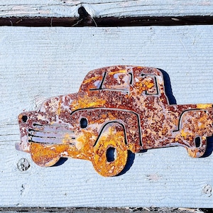 Peut inclure: Une d&eacute;coupe en m&eacute;tal rouill&eacute; d'un camion vintage. Le camion est peint dans des tons d'orange, de brun et de rouge, ce qui lui donne un aspect vieilli et us&eacute;.