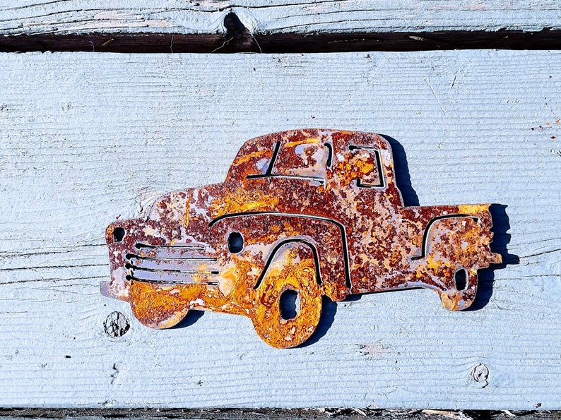 Peut inclure: Une d&eacute;coupe en m&eacute;tal rouill&eacute; d'un camion vintage. Le camion est peint dans des tons d'orange, de brun et de rouge, ce qui lui donne un aspect vieilli et us&eacute;.