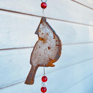 May include: A rusty metal cardinal bird silhouette hanging from a wire with red and clear glass beads.