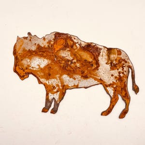 May include: A rusty metal sculpture of a bison, with a white patina on the surface. The sculpture is a silhouette of a bison, with a simple design.