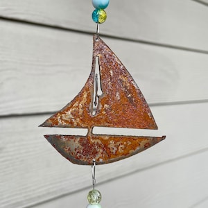 May include: A rusty metal sailboat wind chime with blue, green, and white glass beads hanging from it.